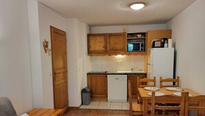 A compact kitchen with wooden cabinets, a microwave, and a dishwasher. There is a dining table with chairs and a grey sofa with a white pillow.