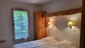 A bedroom with a bed, a window with lace curtains, and two wall-mounted lamps.