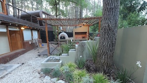 Un espace extérieur rustique agrémenté d’une pergola, d’un barbecue et de diverses plantes et roches.