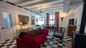 Ein Wohnzimmer mit Schachbrettmuster-Boden, einem roten Sofa, einem Esstisch mit Stühlen, einer Chandelier und einem Fernseher auf einem Schrank.
