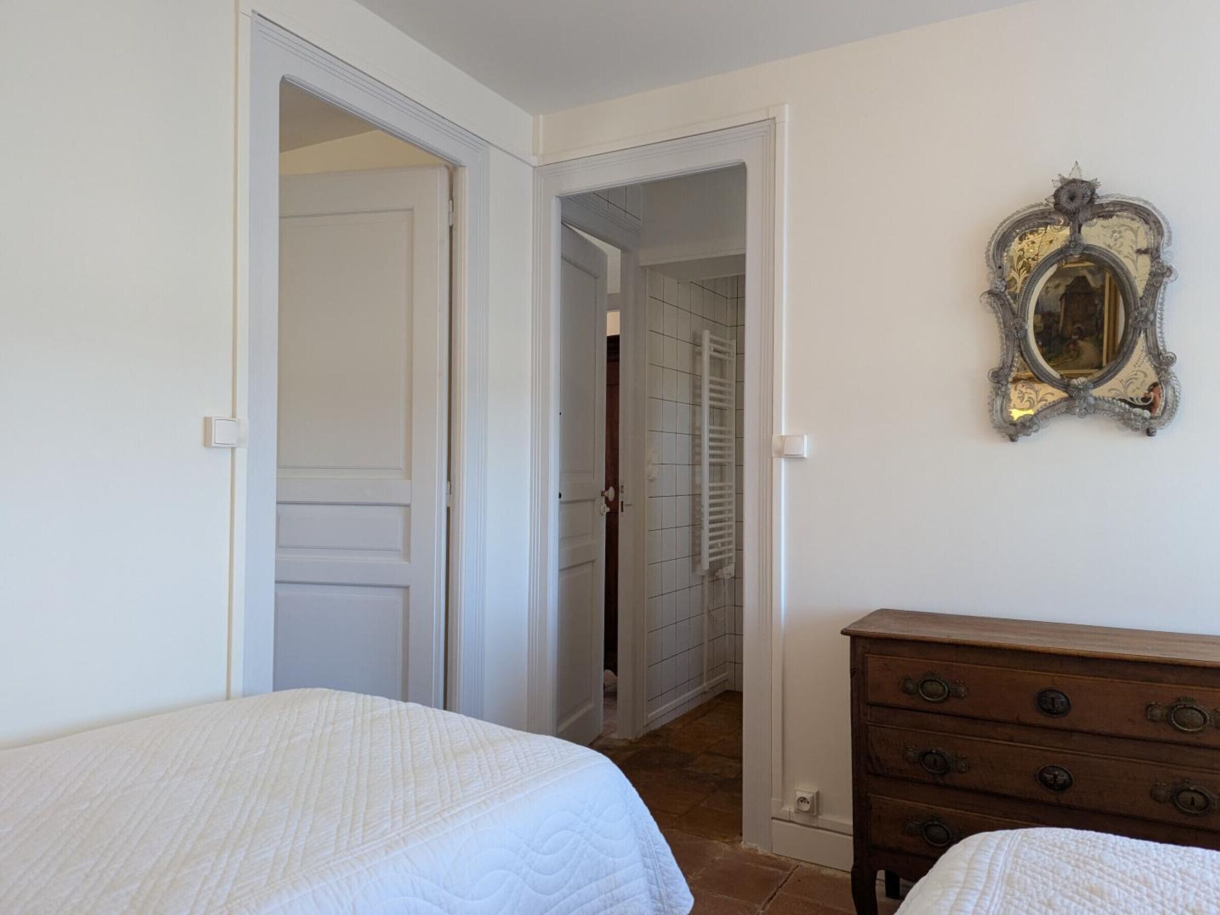 Une chambre avec deux lits, une commode et un miroir au mur.