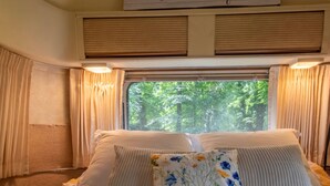 Una cama con muchas almohadas, una ventana con cortinas y un cartel encima, con vista a árboles.