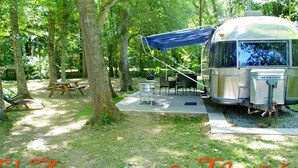 Un camping con una caravana antigua, mesas de picnic y una hamaca.