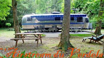 En husbil parkerad på en skogig plats med picknickbord och stolar.
