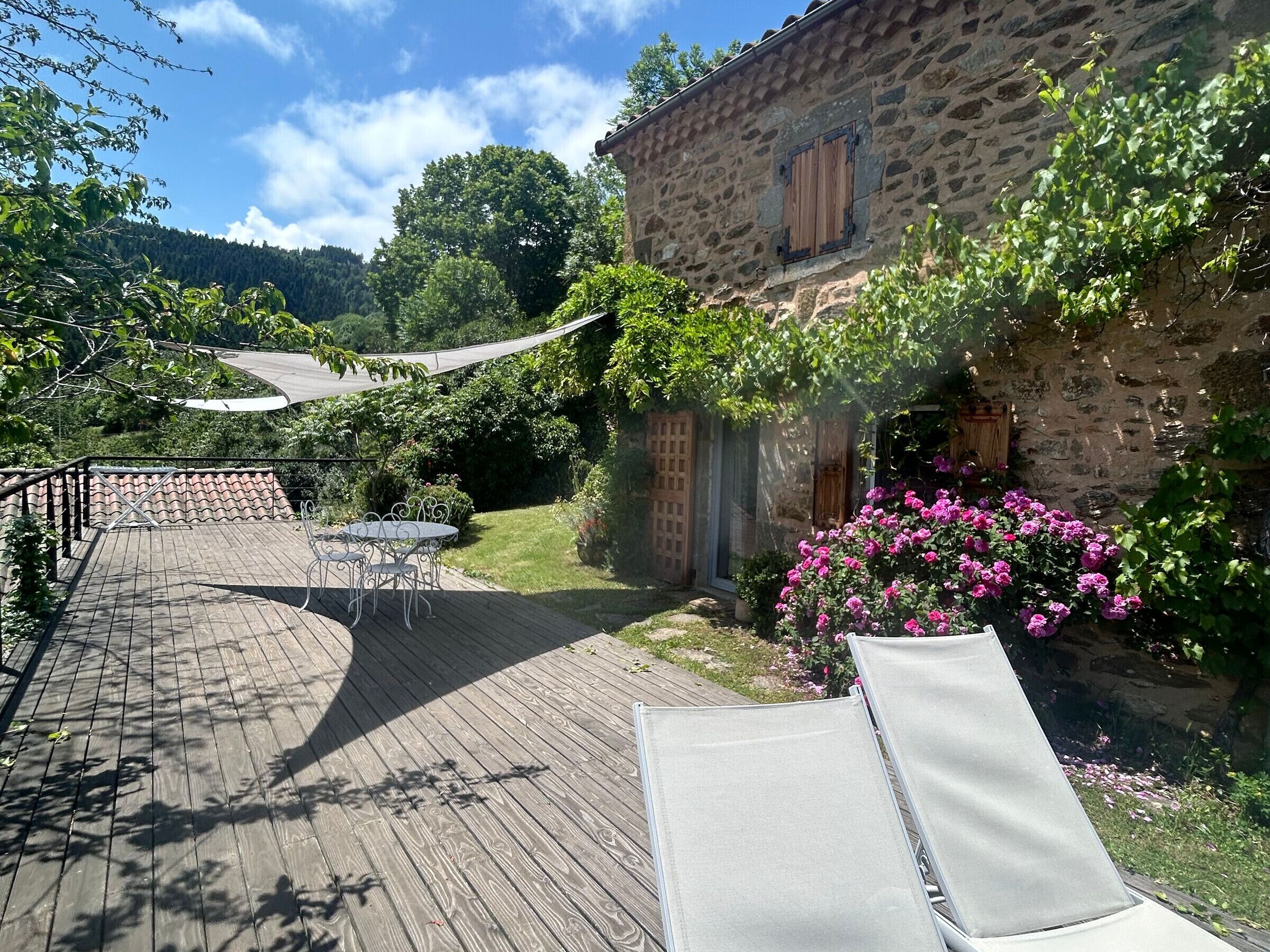 Une terrasse avec une table et des chaises, entourée d’un mur de pierre et d’une végétation luxuriante.