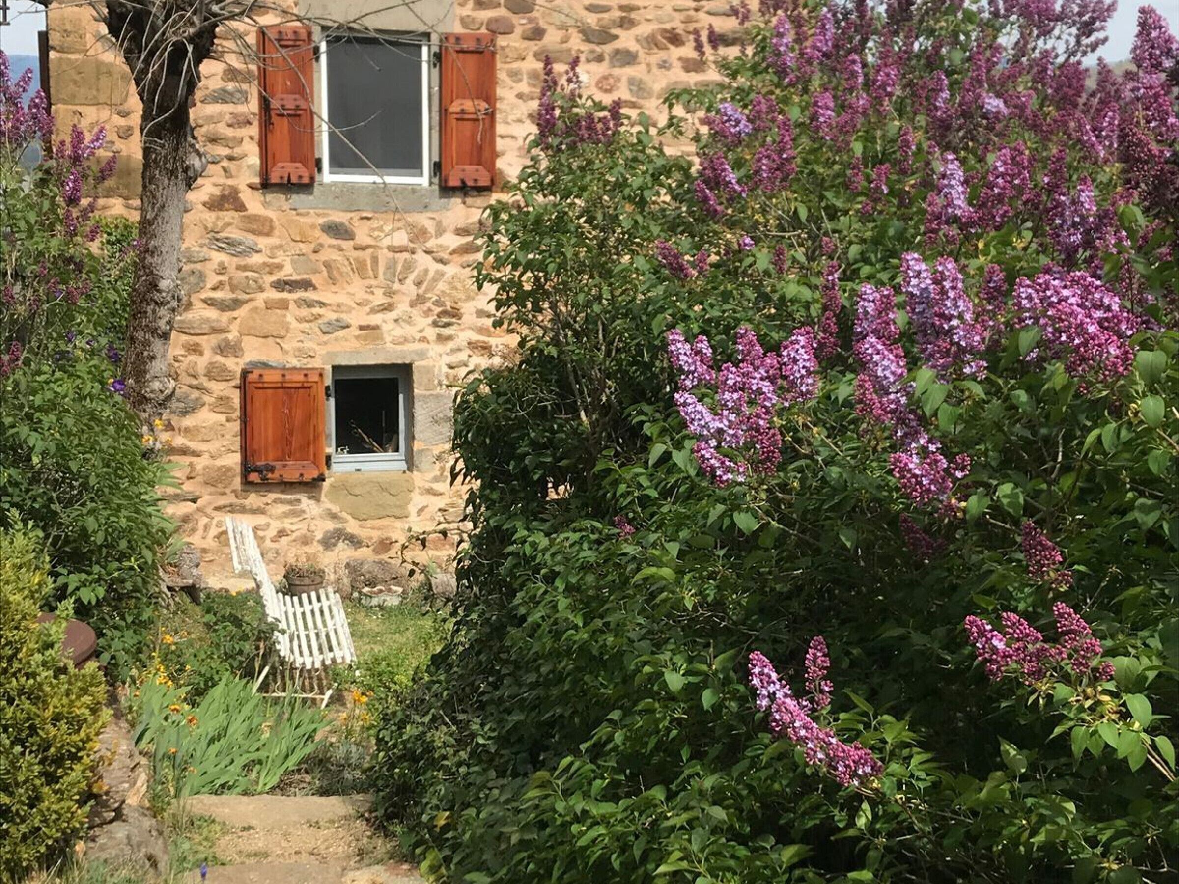 Un edificio de piedra con contraventanas de madera, una ventana pequeña y una silla blanca en el exterior.