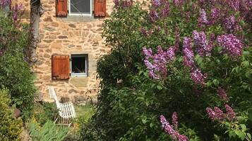 Un edificio de piedra con contraventanas de madera, una ventana pequeña y una silla blanca en el exterior.