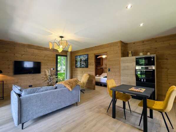 Una sala de estar moderna con un sofá gris, sillas amarillas, una mesa de comedor, un televisor y una pared de madera.