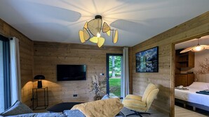 Una sala moderna con sofá, sillón y ventilador de techo. Hay un televisor montado en la pared y un cuadro sobre el sillón.