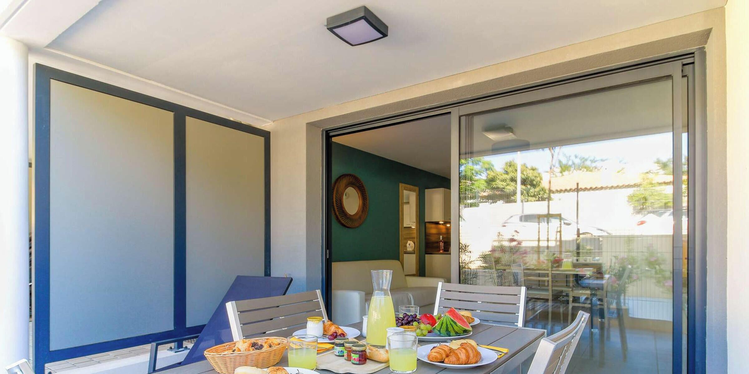 A dining area with a table set for breakfast, including croissants, fruit, and beverages.
