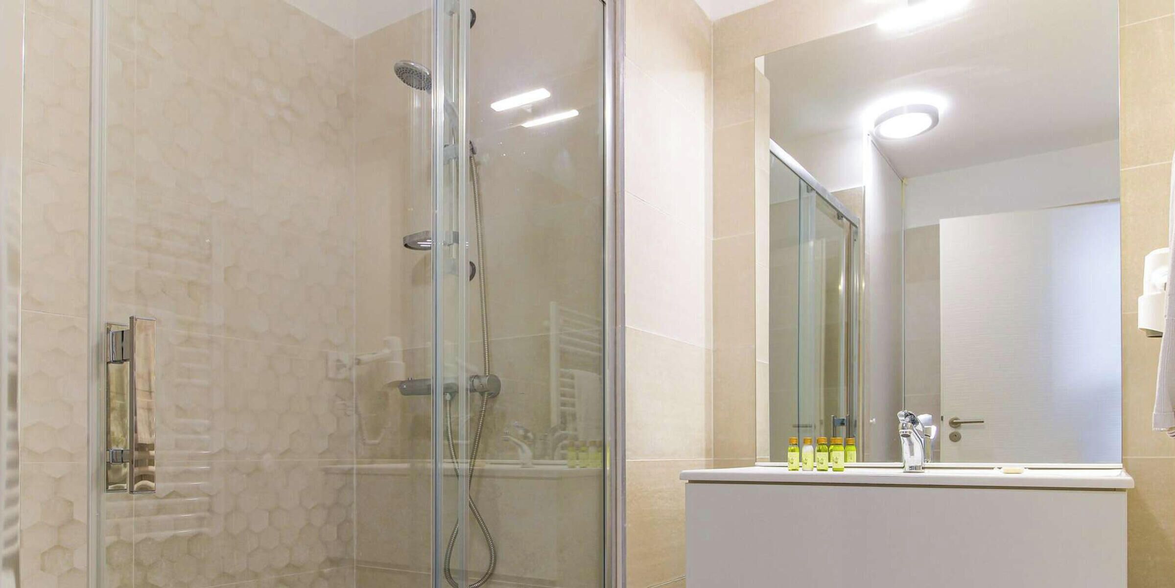 Ein Badezimmer mit einer Duschkabine aus Glas, einem weißen Waschbecken mit Toilettenartikeln und einem großen Spiegel.