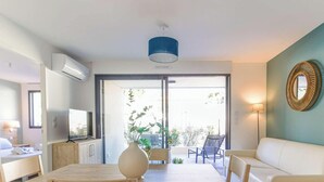 A modern living room with a dining table, chairs, a sofa, and a TV. There is a large window with a view of the outdoors. - Charming apartment in La Favière, pets allowed, near beaches (Bormes-les-Mimosas)