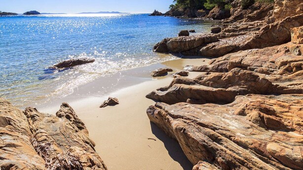 A rocky beach with clear blue water and distant land.