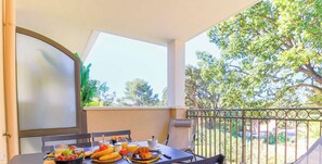 Ein Balkon mit einem für das Frühstück gedeckten Tisch, mit Früchten, Brot und Getränken.