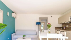 A modern living room with a sofa, a dining table, and a kitchen area. - 2-room apartment with terrace, pool and pets allowed at La Favière (Bormes-les-Mimosas)