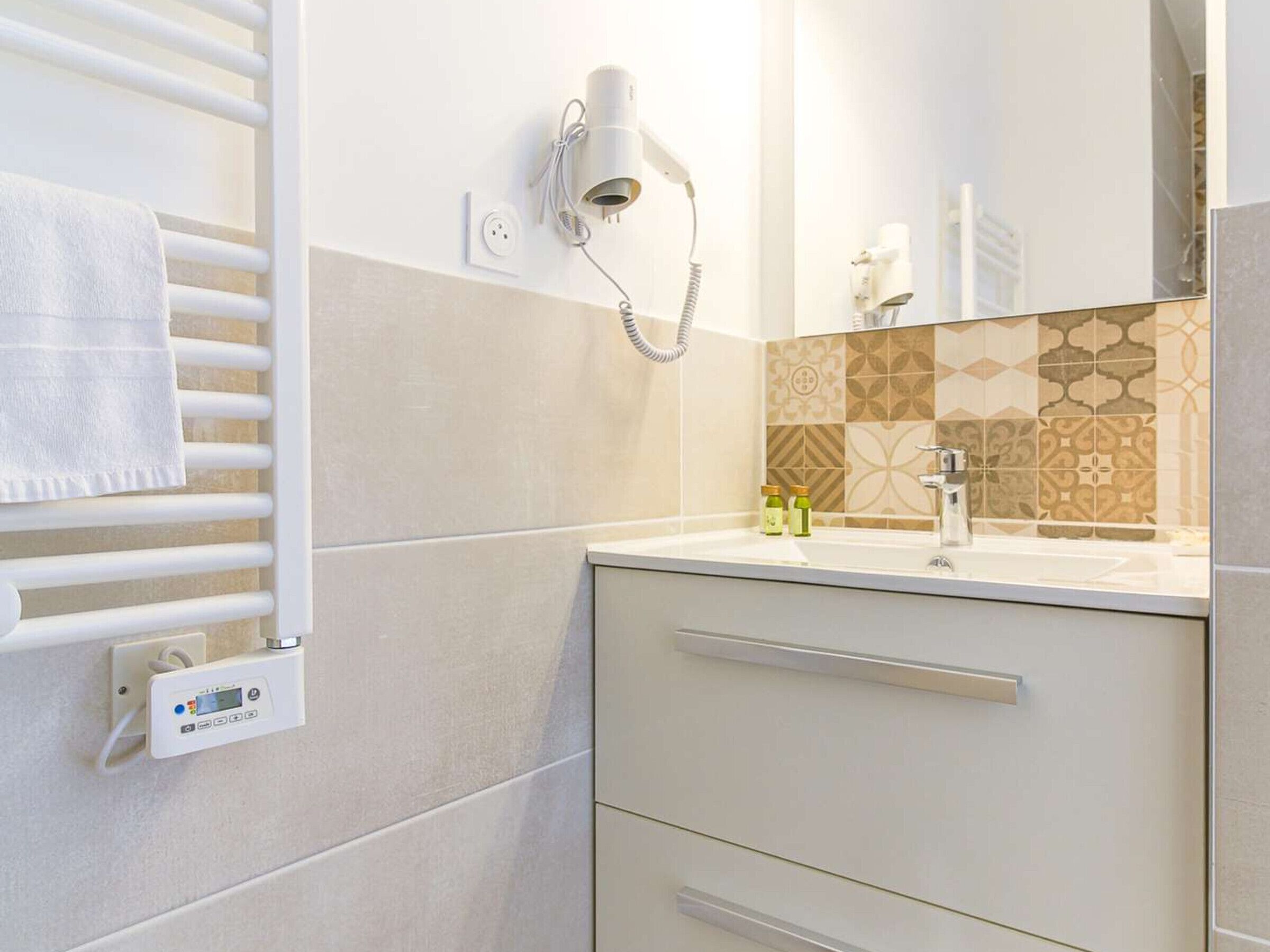 Une salle de bain moderne équipée d’un porte-serviettes, d’un sèche-cheveux, d’un panneau de commande numérique et de carreaux à motifs.