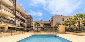 Piscina com pérgola, rodeada por uma cerca, e adjacente a edifícios com varandas.