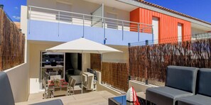 Un bâtiment à deux étages doté d’un balcon, d’un espace repas avec mobilier d’extérieur et d’un coin salon abrité.