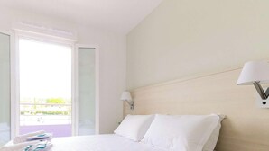 Habitación de hotel con cama, mesita de noche, lámpara y vistas al exterior.