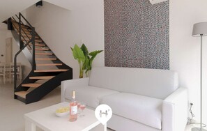 Un salon moderne avec un canapé blanc, une table basse sur laquelle se trouvent une bouteille et des verres, un escalier avec des marches en bois et un mur à motifs.
