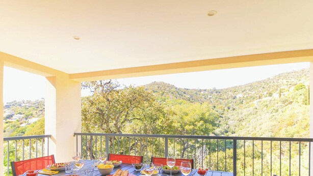 A balcony with a table set for dining, overlooking a mountainous landscape.