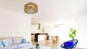 A modern living room with a sofa, a coffee table, and a blue chair. There is a kitchen in the background with a dining area.