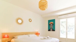 A bedroom with a bed, two wall mirrors, a painting, a window, and a chair.