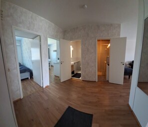 Amplia habitación con piso de madera, un tapete negro y un baño visible con ducha.