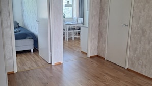 Een kamer met een houten vloer, een zwarte deurmat en een bed met grijze beddengoed.