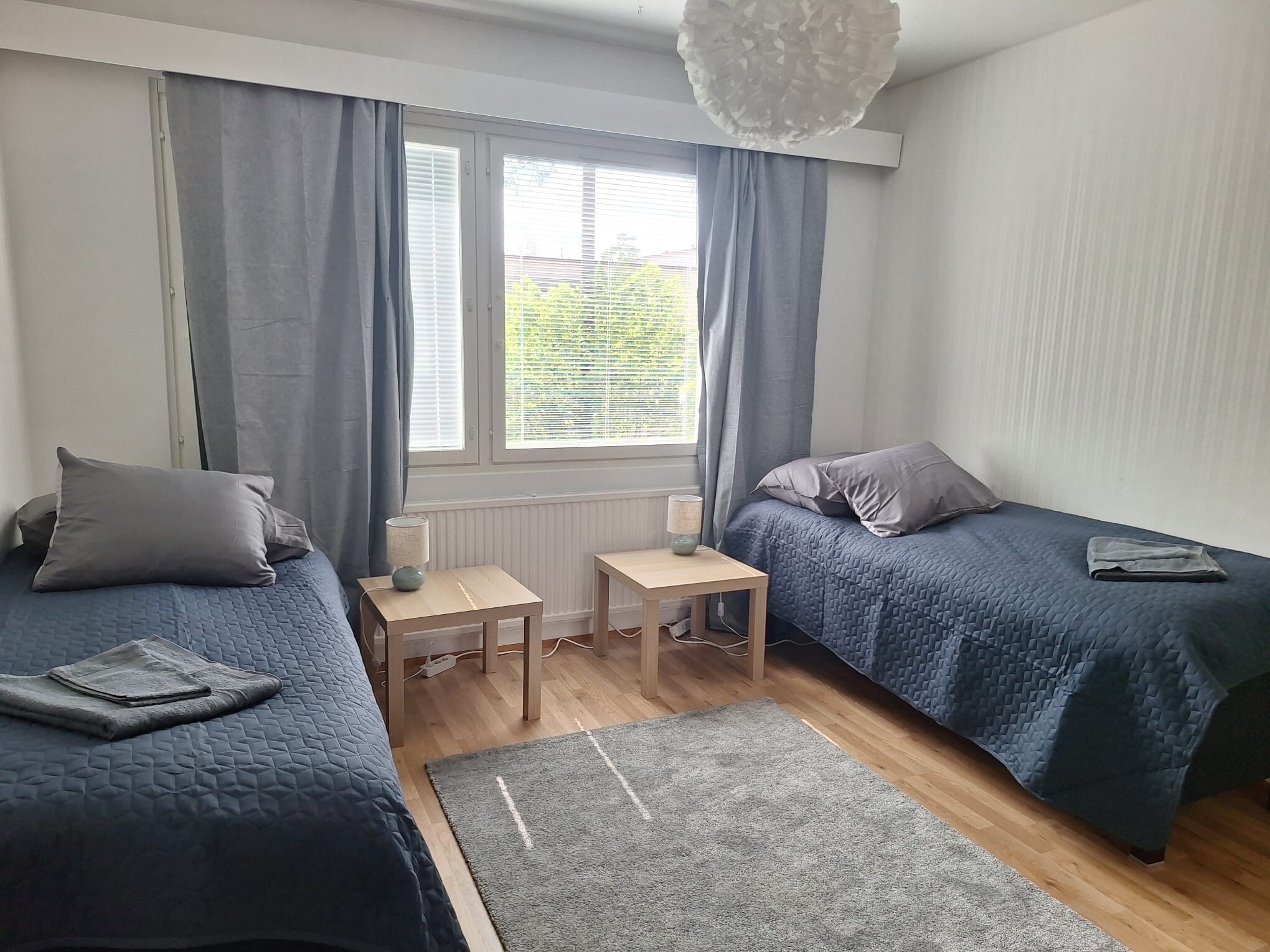 Ein Schlafzimmer mit zwei Betten, einem kleinen Tisch, einer Lampe und einem Fenster mit Vorhängen.