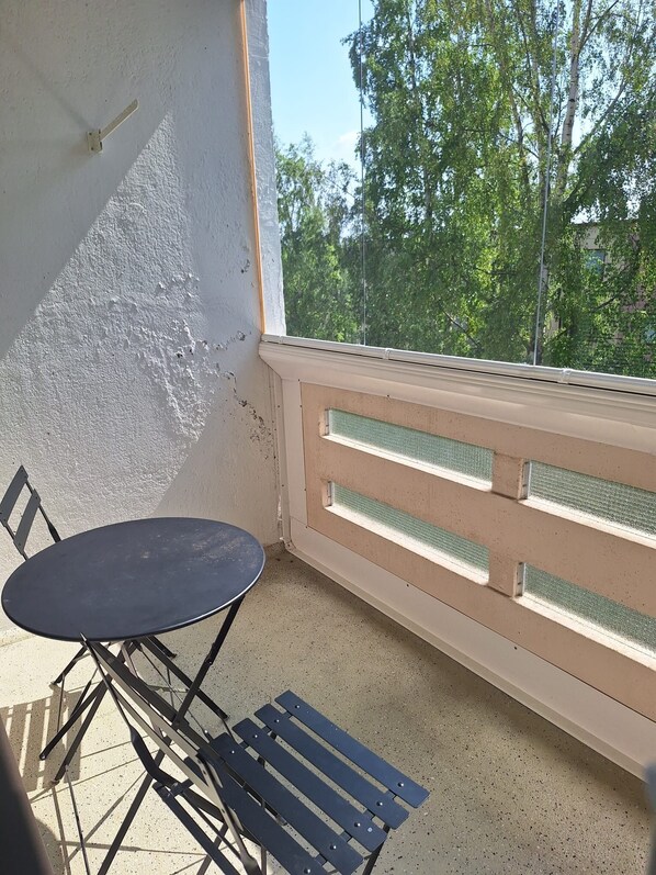 A balcony with a table and chairs, a railing, and a view of trees and buildings.