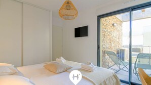 A bedroom with a bed, a television, a wicker pendant light, and a sliding glass door leading to an outdoor area with chairs. - Modern T3 with Lovely Terrace in Bormes-les-Mimosas (Bormes-les-Mimosas)