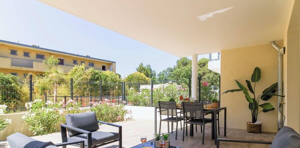 An outdoor patio with a table and chairs, surrounded by plants and a view of a building.