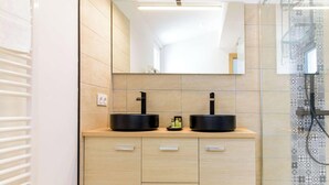Une salle de bain moderne avec deux lavabos noirs, un miroir et une zone de douche au motif décoratif.