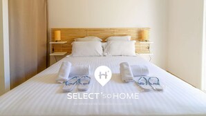 Un lit bien fait, avec du linge de lit et des serviettes blanches, une tête de lit en bois et une table de chevet avec une lampe.