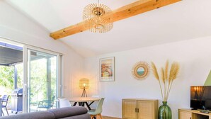 Un salon moderne avec un canapé gris, une table ronde en bois, un téléviseur et un coin repas comprenant des chaises et une lampe.