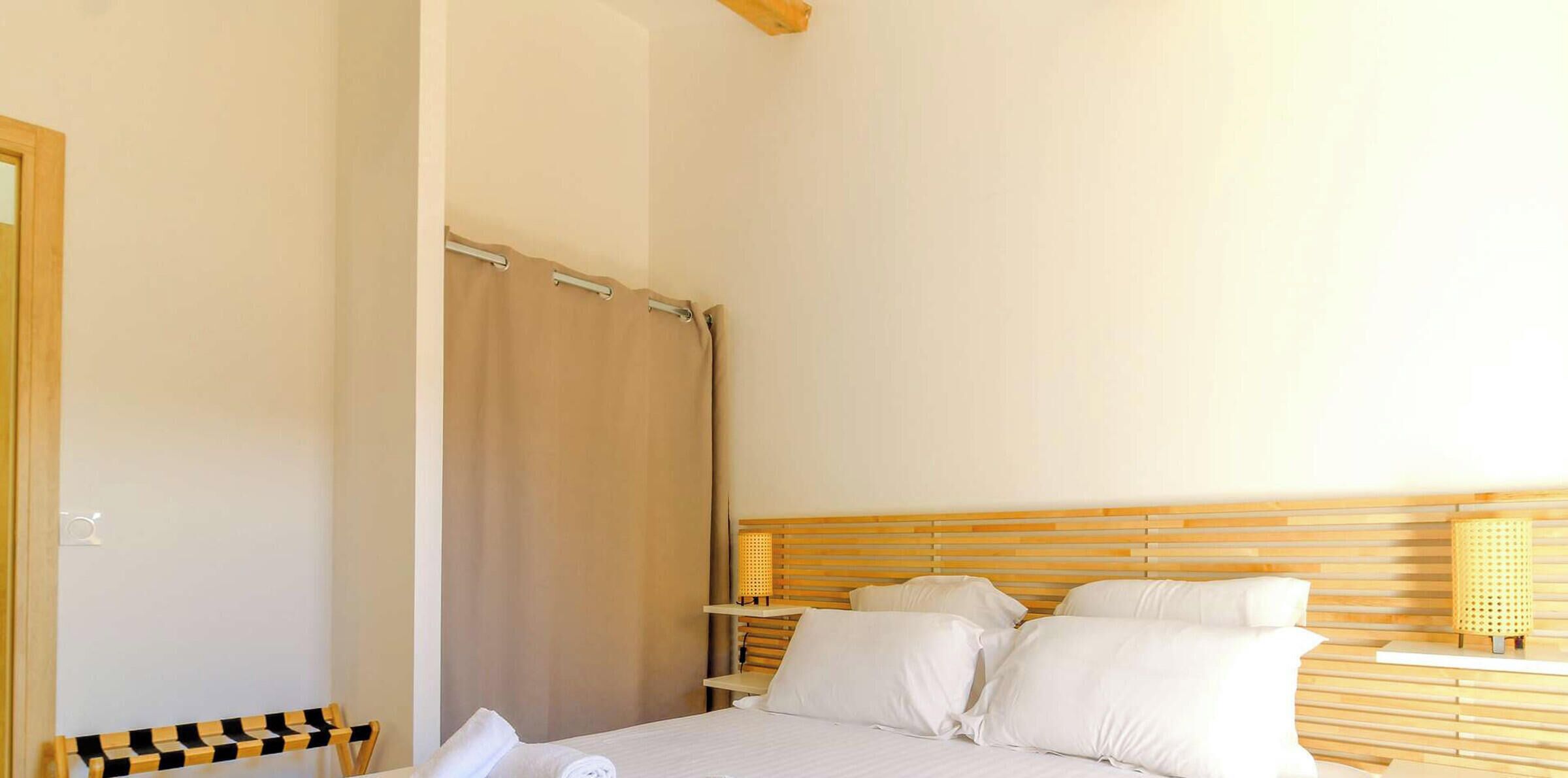 Quarto com cama, cabeceira de madeira, mesa de cabeceira e cortina.