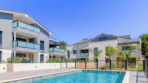 A modern residential building with a swimming pool, balconies, and a clear sky.