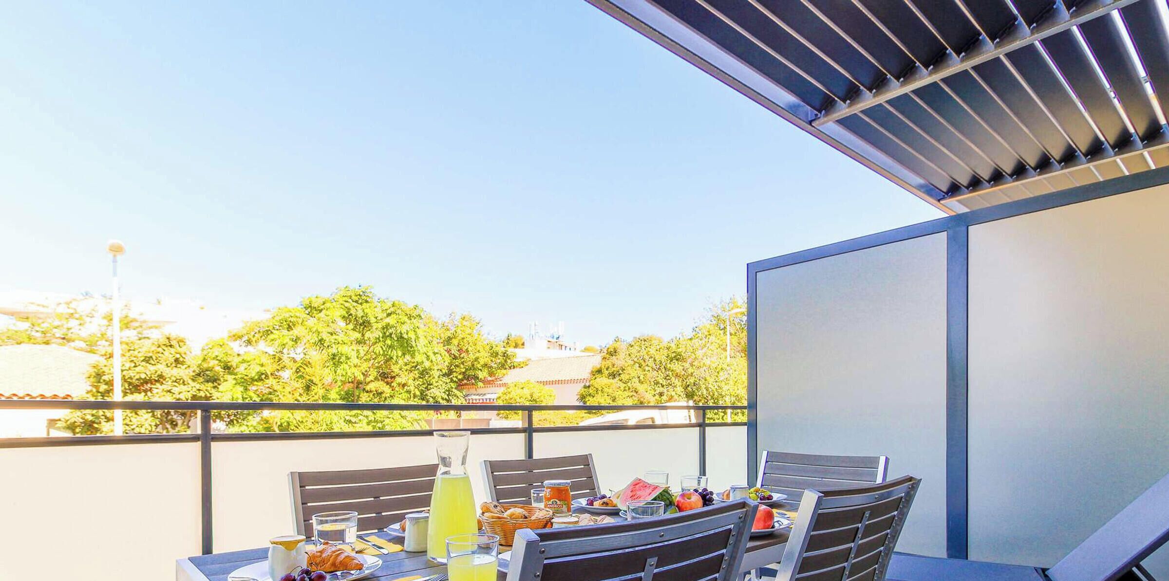 Een balkon met een ontbijttafel, compleet met croissants, fruit en drankjes.