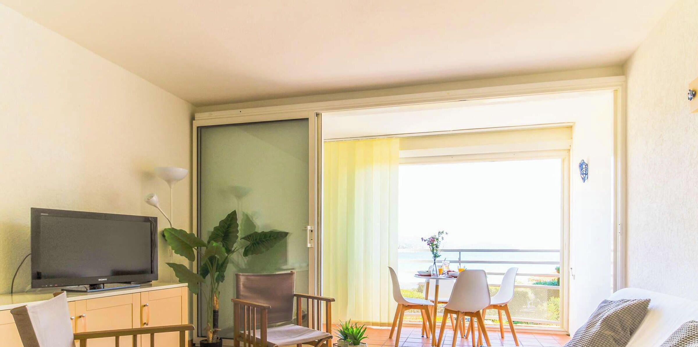 Un salon confortable avec un canapé, des fauteuils, un téléviseur et un balcon agrémenté d’une table et de chaises.