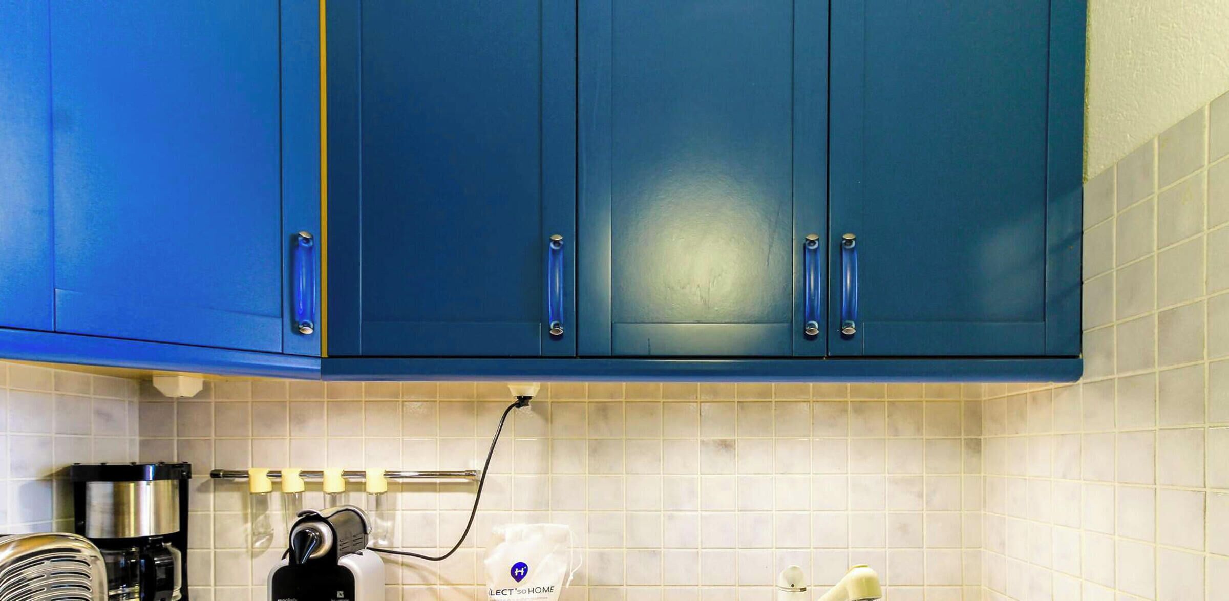 A kitchen with blue cabinets, a coffee maker, and a hairdryer plugged in.