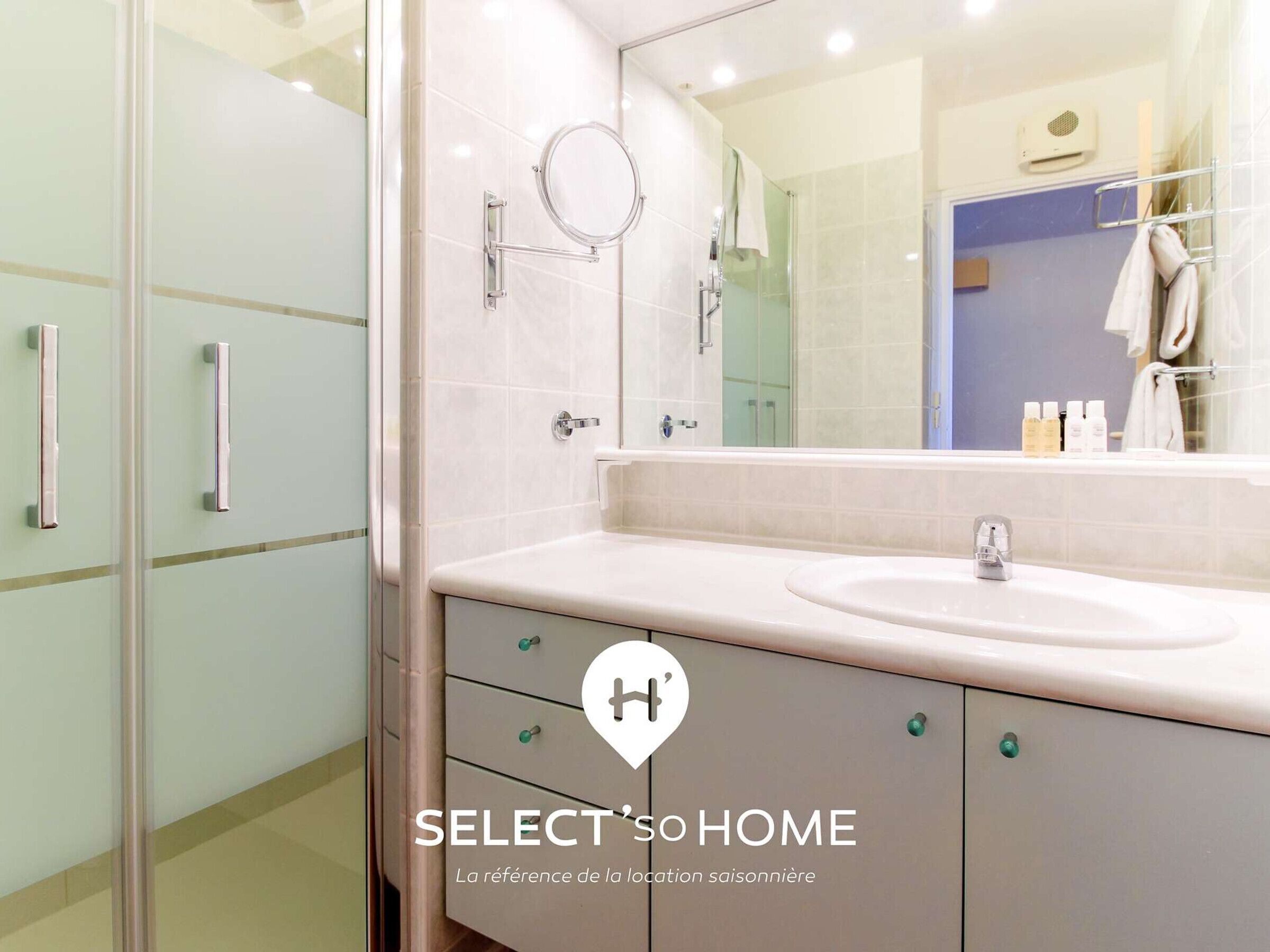 Une salle de bain avec une douche à parois de verre, un miroir rond, un lavabo blanc et un porte-serviettes.