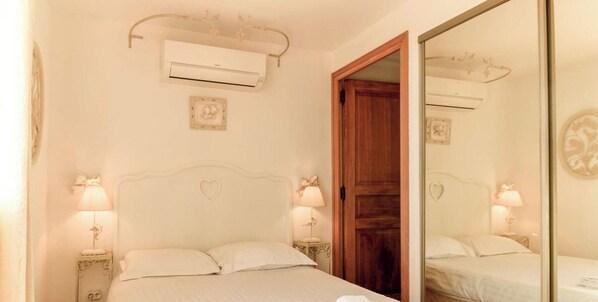 Un dormitorio con cama, lámparas de noche, un espejo, una puerta de madera y un equipo de aire acondicionado.