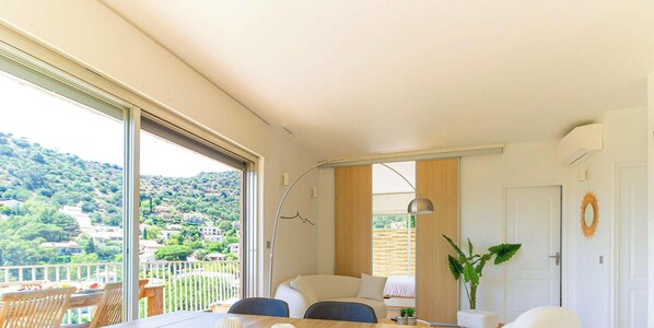 A modern bedroom with a large window, a bed, a desk, and a view of a hillside. - Bright apartment with large terrace, sea view, in Le Lavandou (Le Lavandou)