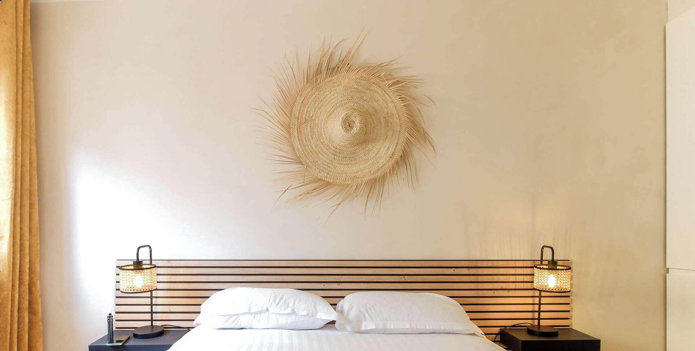 A bedroom with a bed, two bedside lamps, and a woven wall decoration.