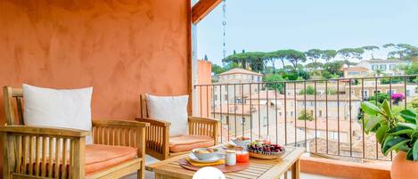A balcony with wooden furniture, a table with food, and a view of buildings and trees.