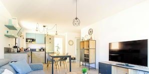 En moderne stue med et fladskærms-tv, et spisebord med stole, en sofa og et køkken med mikrobølgeovn og komfur.