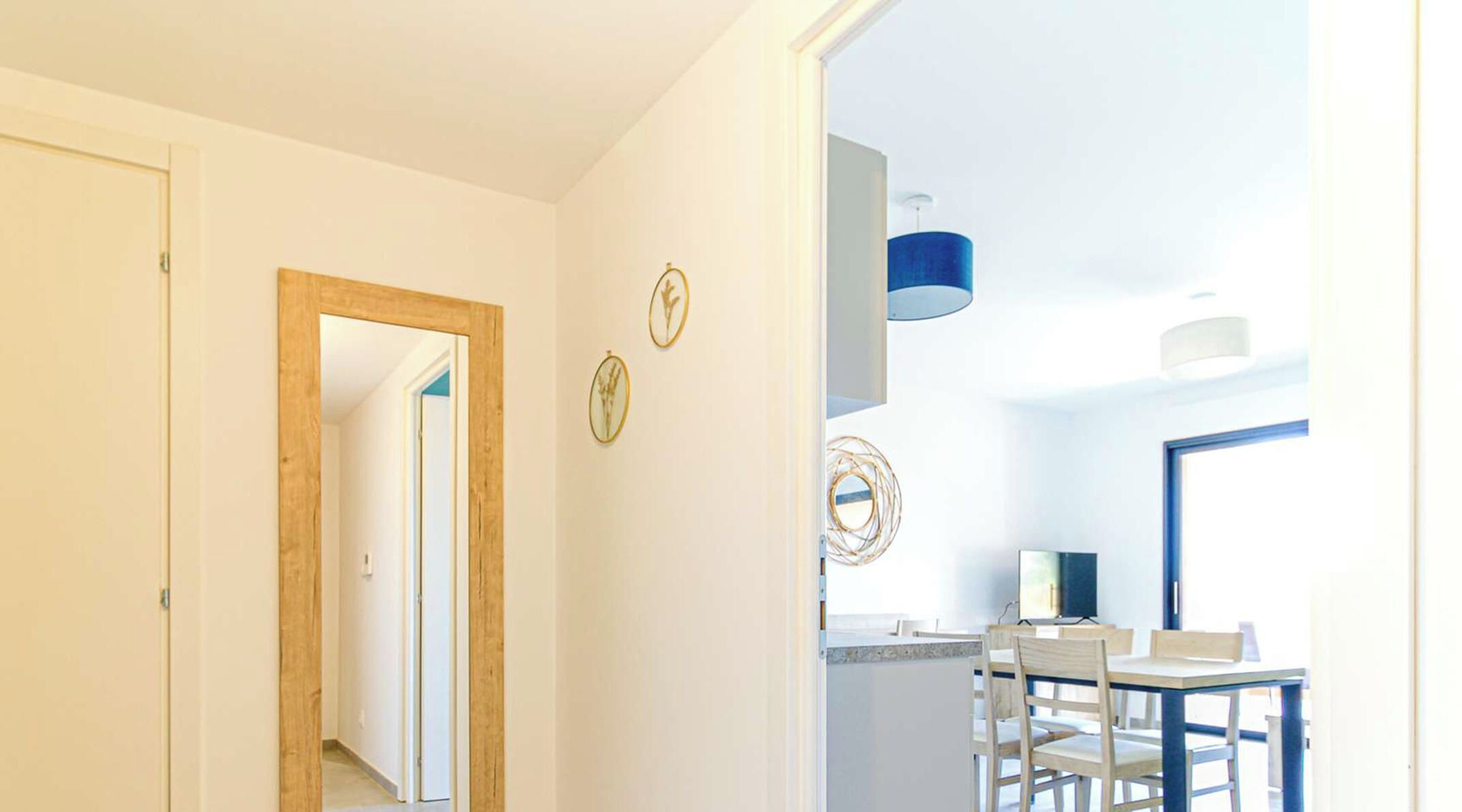 A hallway leading to a dining area with a table and chairs, a blue ceiling light, and a door on the left.