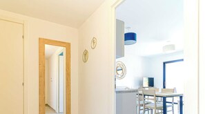 Un pasillo que conduce a un comedor con una mesa y sillas, una lámpara de techo azul y una puerta a la izquierda.