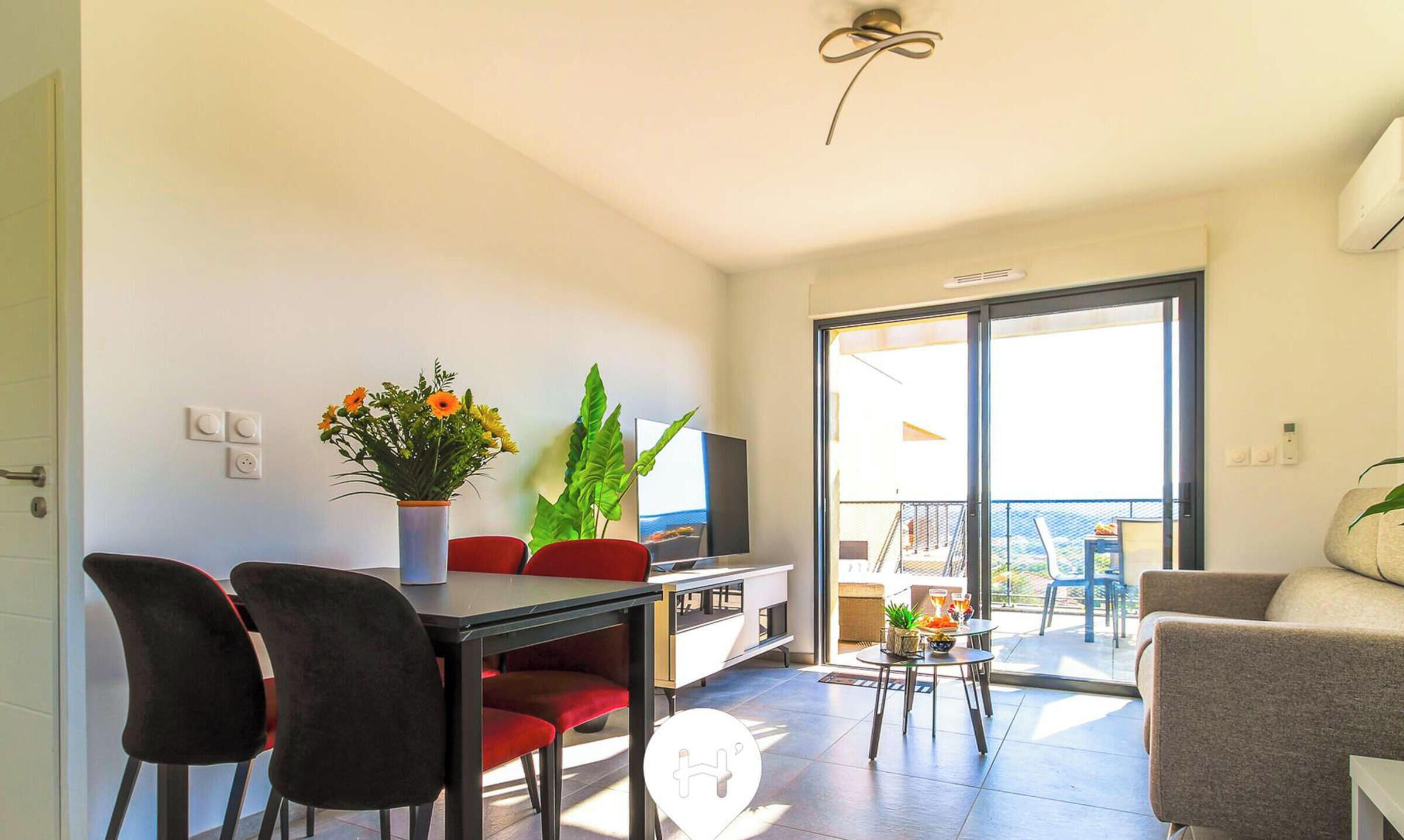 A modern living room with a dining area, a TV, and a balcony with a view.